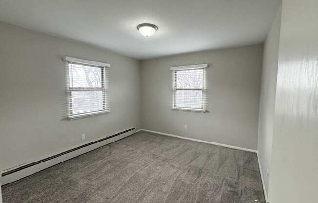 an empty bedroom with a carpeted floor and two windows