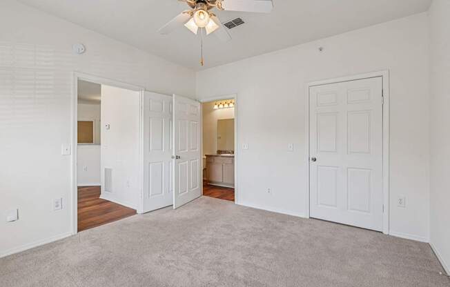 A spacious bedroom with a ceiling fan, carpeted floor and attached bathroom