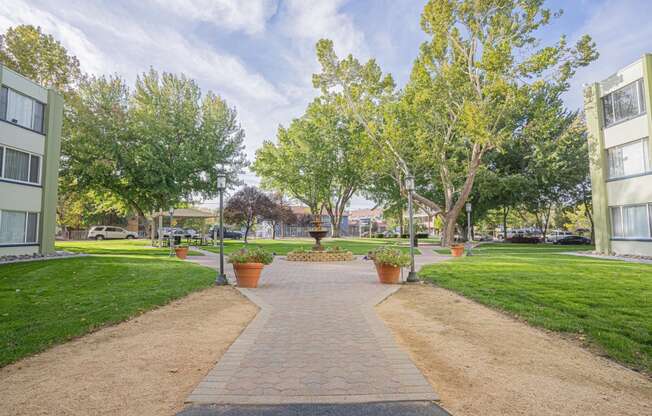 a walkway through a park between two buildings with grass and trees