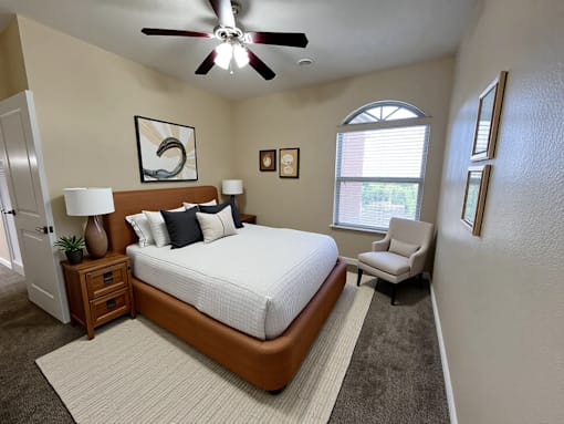 A bedroom with a large bed, a ceiling fan, and a window with blinds.