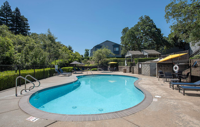A pool surrounded by a black fence and trees at Rocklin Gold Apartments, California, 95677