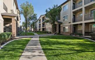 a walkway between two apartment buildings with grass and trees