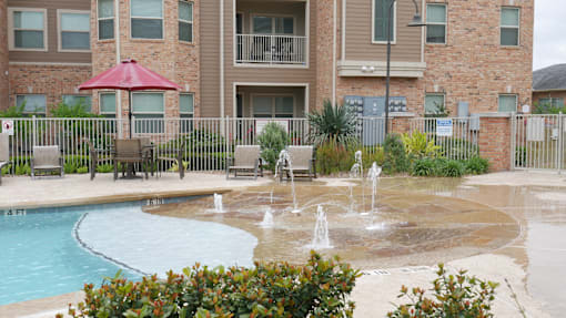 A pool with a fountain in front of a brick building.