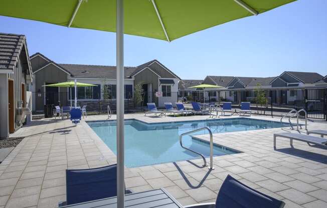 a swimming pool with chairs and umbrellas in front of a house at Village of Chandler Apartments, Chandler, Arizona