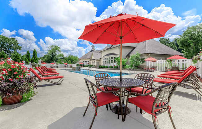 A red umbrella shades a table with chairs around a pool.