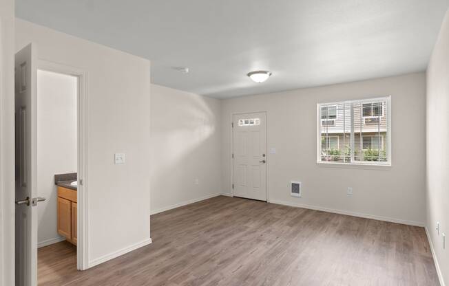 the living room of an apartment with wood flooring and a door to the kitchen