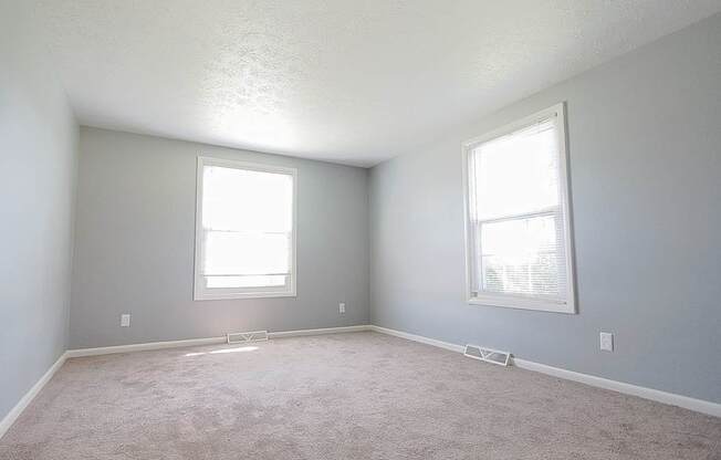 A room with two windows and carpeted floor.