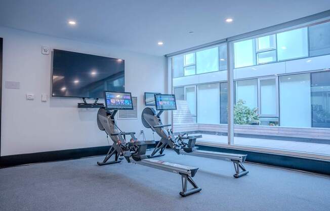 A room with a television, two exercise bikes, and a bench.