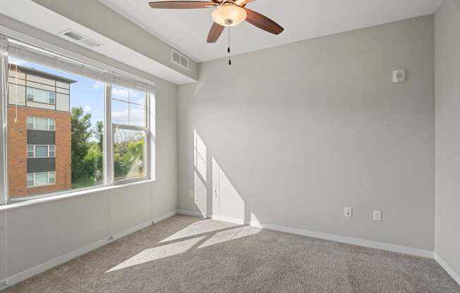 A room with a ceiling fan and a window overlooking a building.
