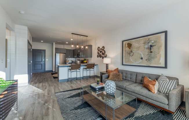 A modern living room with a grey couch and a large abstract painting on the wall.