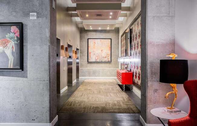 a hallway with a rug and paintings on the wall and a red chair and table