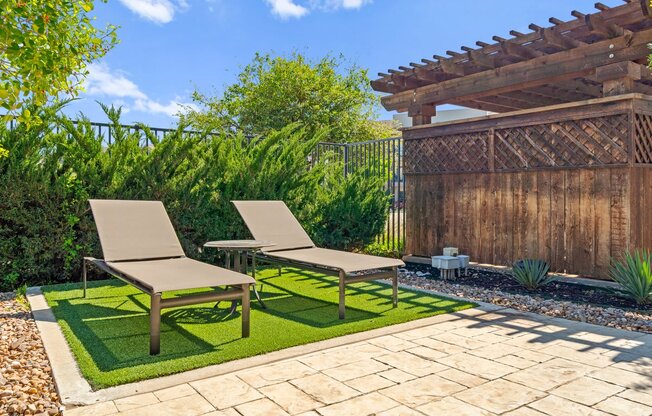 a patio with two lounge chairs and a table on grass