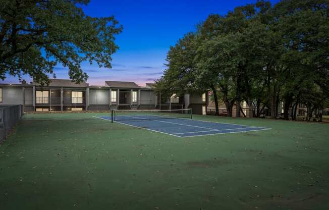 a tennis court in front of a building with trees