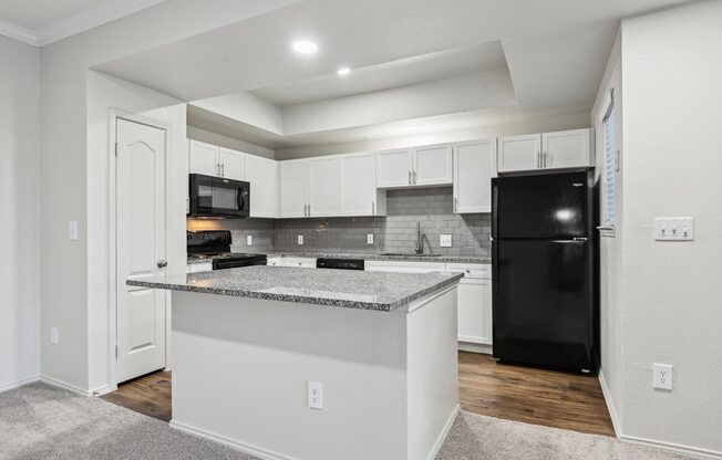 A kitchen with a black refrigerator and white cabinets.