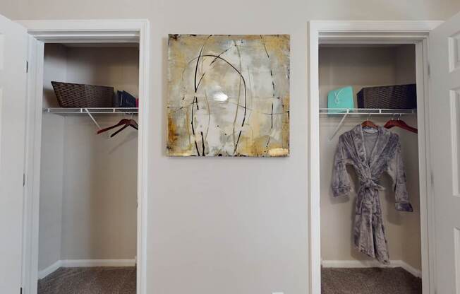 A room with two open closets and a painting on the wall.