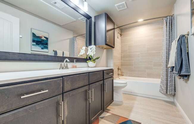 A bathroom with a white toilet, a sink with a mirror above it, and a bathtub with a shower curtain.