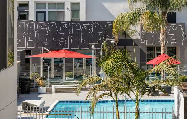 A pool surrounded by palm trees and red umbrellas.