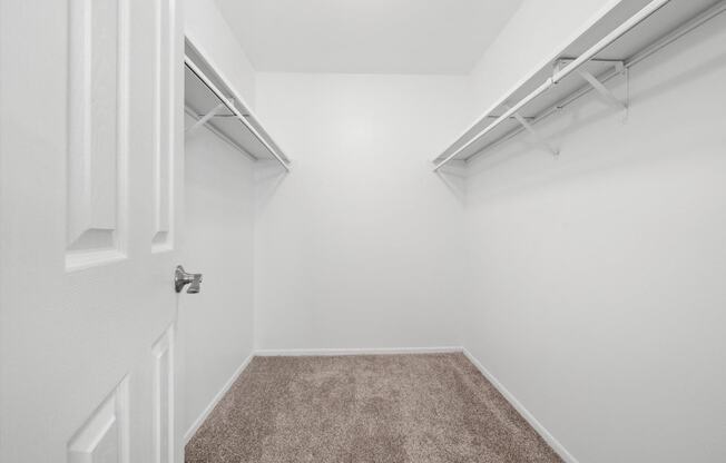 a walk in closet in a home with white walls and a carpet