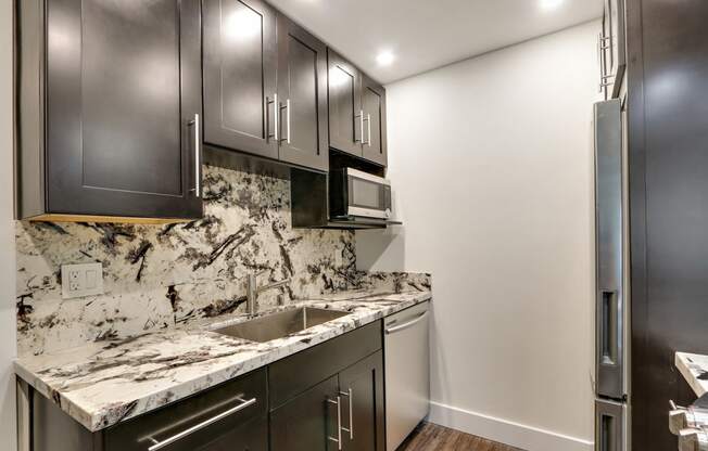 Kitchen with granite countertops and backsplash, stainless steel dishwasher, dishwasher, dark brown kitchen cabinets, wood style floors, two door refrigerator.