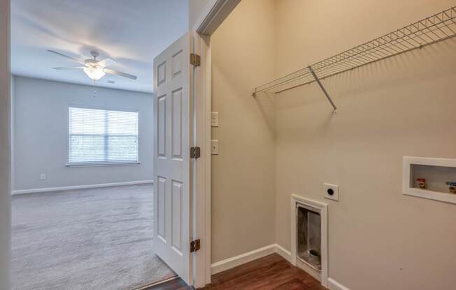 A room with a white door, a window with blinds, a ceiling fan, and a shelf with some items.