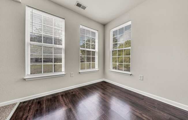 the living room of a new home with wood flooring and three windows