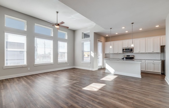 Houston, TX, Rental Homes - East Heights - Unfurnished Living Room with Vinyl Plank Flooring, Ceiling Fan, Large Windows, and View of Kitchen.