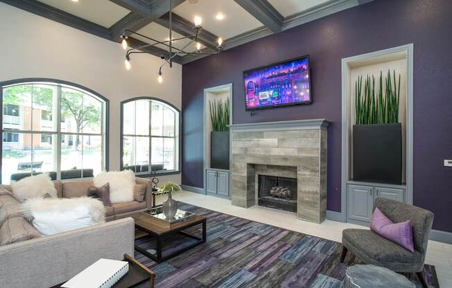 A living room with a grey couch, a coffee table, a fireplace, and a flat screen TV mounted on the wall.