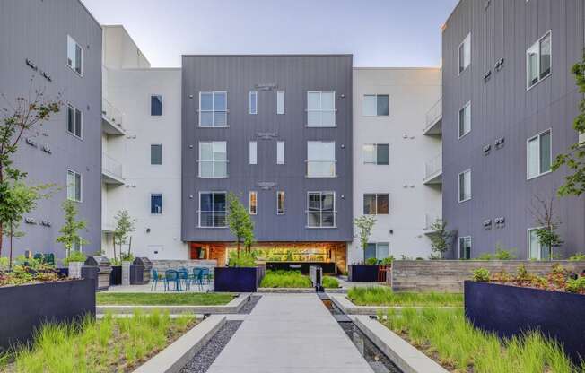 a walkway with benches and tables in front of an apartment building