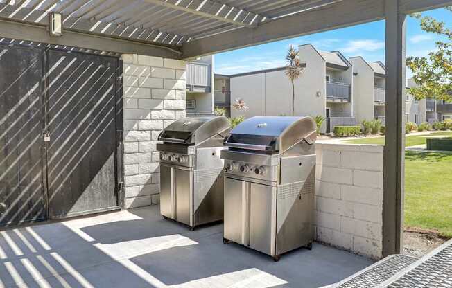 Two stainless steel barbecues are placed under a covered patio area.