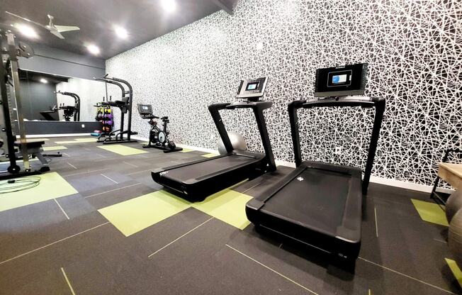 a gym with treadmills and weights on the floor and a wall of wallpaper