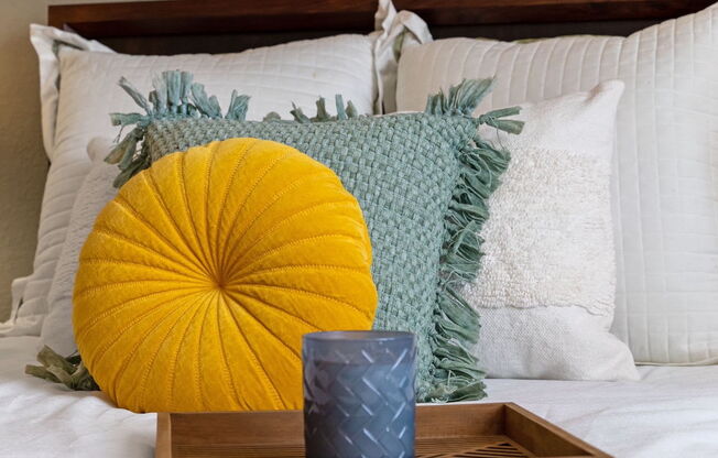 comfortable bed with fluffy white and colored pillows with a tray and candle on a bed