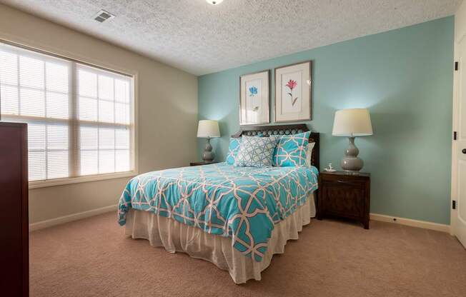 A bedroom with a bed, two lamps, and two framed pictures on the wall.