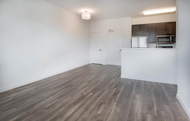 an empty living room with a kitchen in the background