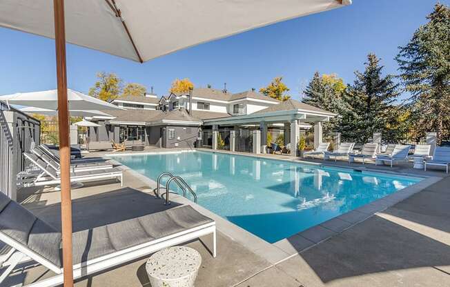 a swimming pool with chairs and umbrellas in front of a house