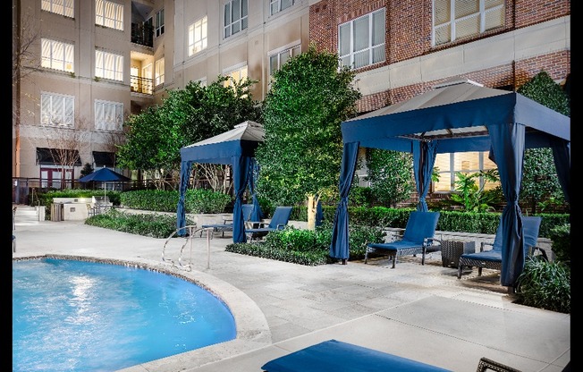 Two blue fabric poolside cabanas in a landscaped courtyard with two blue lounge chairs each.