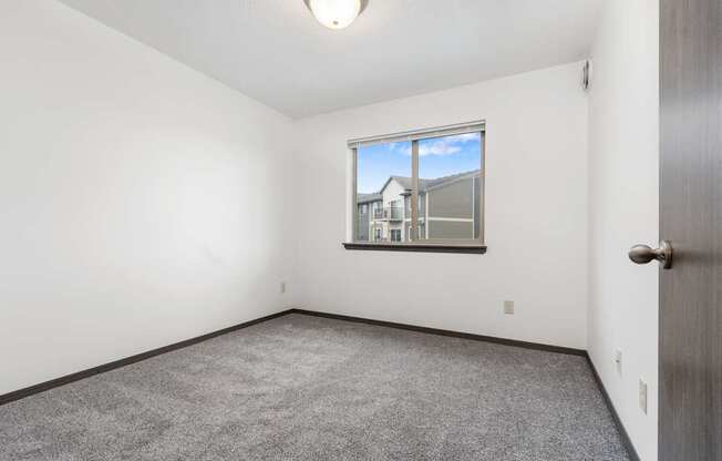 A room with a carpeted floor and a window showing a building outside.