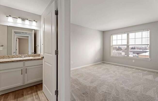 A carpeted room with a window and a bathroom visible through the door.