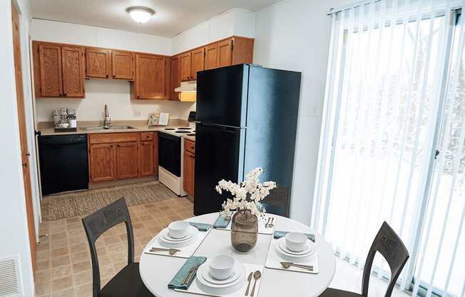 A kitchen with a table set for two and a vase of flowers on the table.
