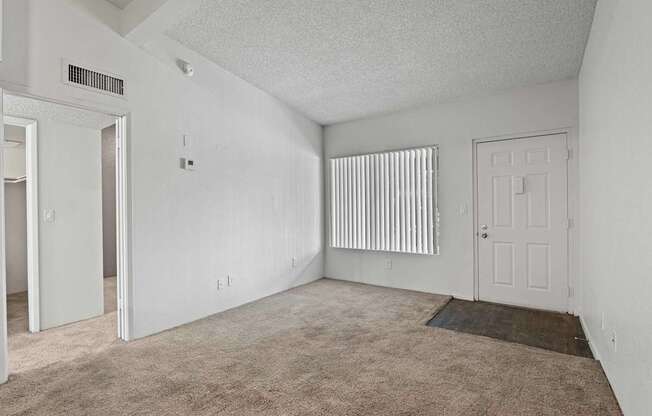 A room with a carpeted floor and a window with blinds.