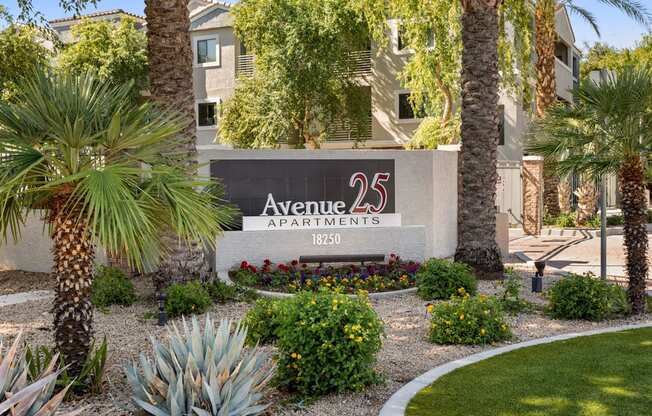 A sign for Avenue 25 Apartments is surrounded by plants and trees.