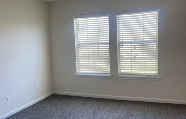 an empty living room with two windows and carpet