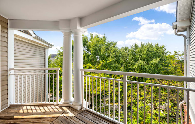 the view from the deck of a home with white columns and a view of trees