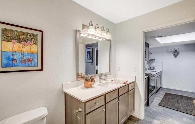 A bathroom with a white sink and a painting of a beach scene.