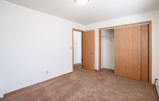 A room with a brown carpet and two wooden doors. Fargo, ND Birchwood 2 Apartments