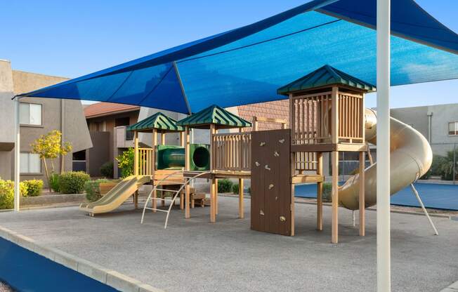 a playground with a slide and a table and chairs under a blue awning