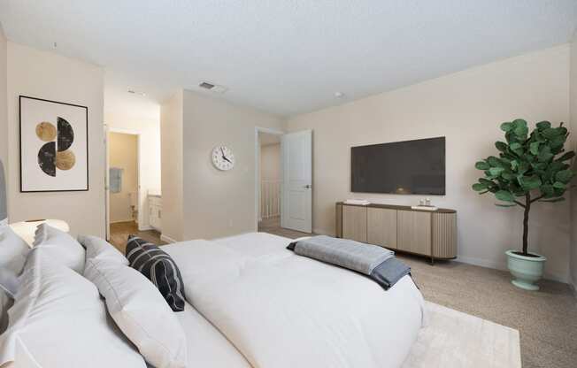 Primary bedroom in the townhouse floor plan with white bed console table and tv on the wall.