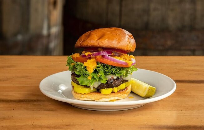 A burger with lettuce, tomato, pickles, and onions is on a plate.