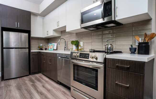 Apartments In DTLA For Rent - Kitchen With Stainless-Steel Appliances, White Cabinets, And Wood-Style Floors