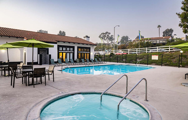 A pool with a hot tub and chairs in front of a house.