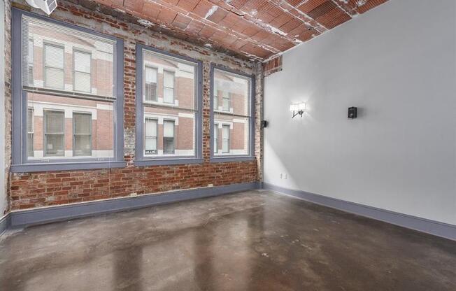 an empty room with a brick wall and three large windows